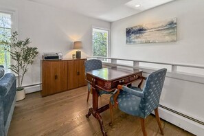 Un coin repas avec une table en bois, deux chaises, un meuble contenant une radio et un tableau accroché au mur.