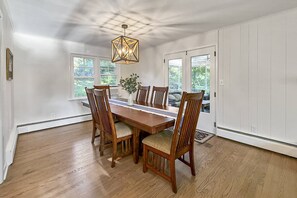 Comedor con mesa y sillas de madera, lámpara colgante y ventanas con vistas a zonas verdes.