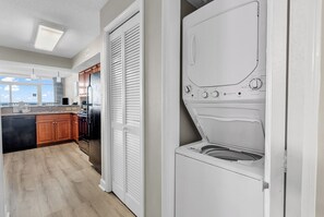 A laundry room with a front-loading washer and dryer, wooden cabinets, and a view to the outside. - Dunes Village Oceanfront Condo + Waterpark (Myrtle Beach)