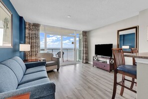 A hotel room with a sofa, a TV, a dining table with chairs, and a balcony with a view of the sea. - Dunes Village Oceanfront Condo + Waterpark (Myrtle Beach)