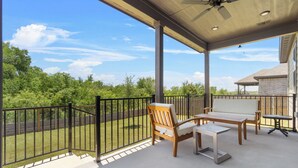 Eine überdachte Terrasse im Freien mit Tisch und Stühlen, einem Deckenventilator und Blick auf eine grüne Landschaft.