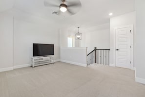 A spacious living room with a flat-screen TV on a white entertainment unit, a ceiling fan, and a staircase with a black railing. - Fully furnished and appointed home for corporate lease.   All utilities paid. (Manor)