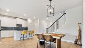 Eine moderne Küche mit weißen Schränken, einem Holztisch mit vier Stühlen und einer Treppe mit Geländer.