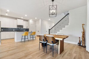 A modern kitchen with white cabinets, a wooden dining table with four chairs, and a staircase with a railing. - Fully furnished and appointed home for corporate lease.   All utilities paid. (Manor)