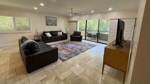 A spacious living room with a large window, a ceiling fan, and a flat-screen TV on a wooden stand. - 3 bedroom condo fully updated- Innisbrook Resort (Palm Harbor)