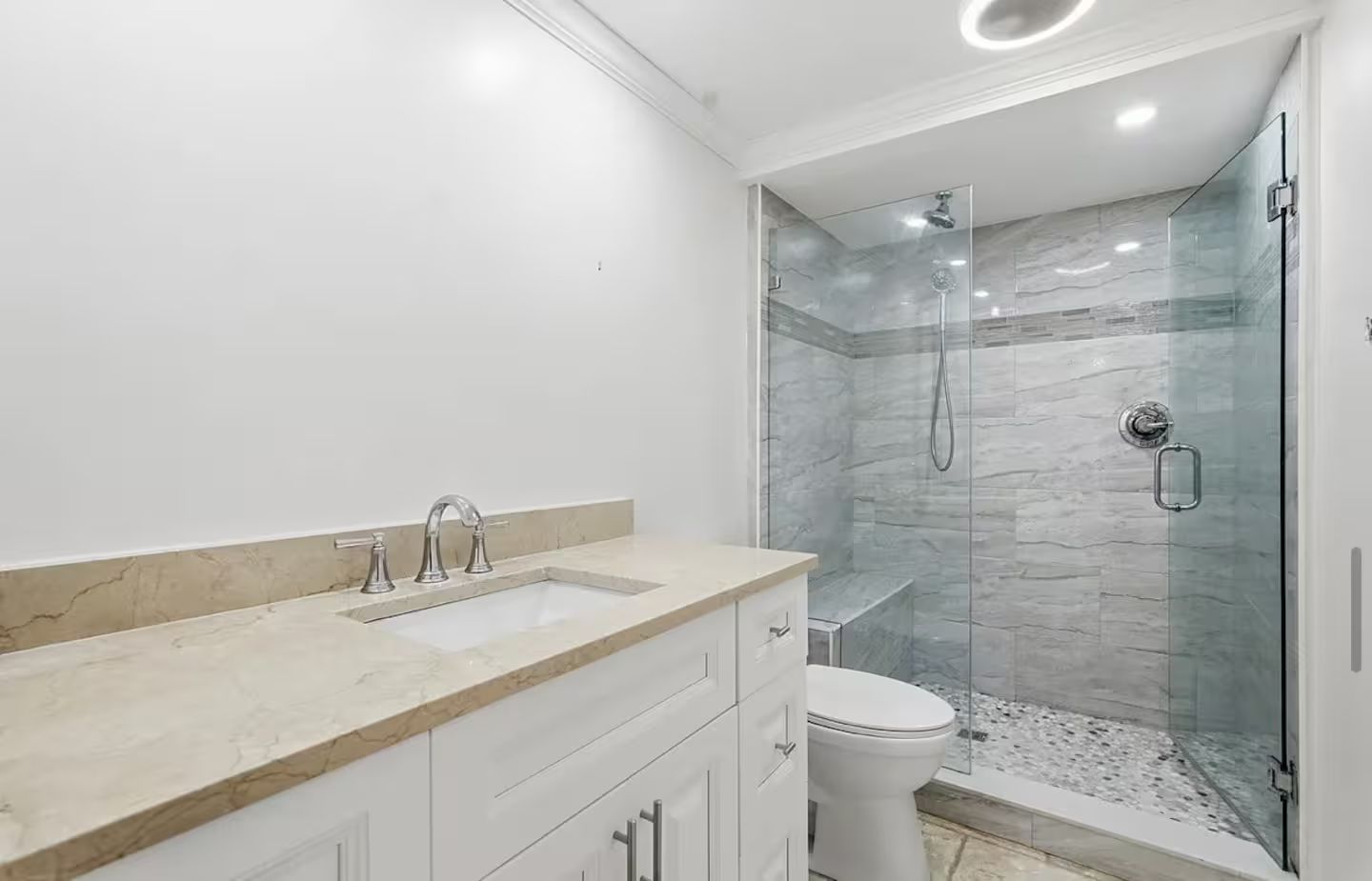 A modern bathroom with a glass-enclosed shower, a white toilet, and a marble vanity.