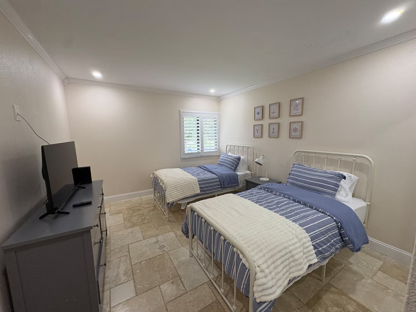 Un dormitorio con dos camas, televisión y ventana con persianas.