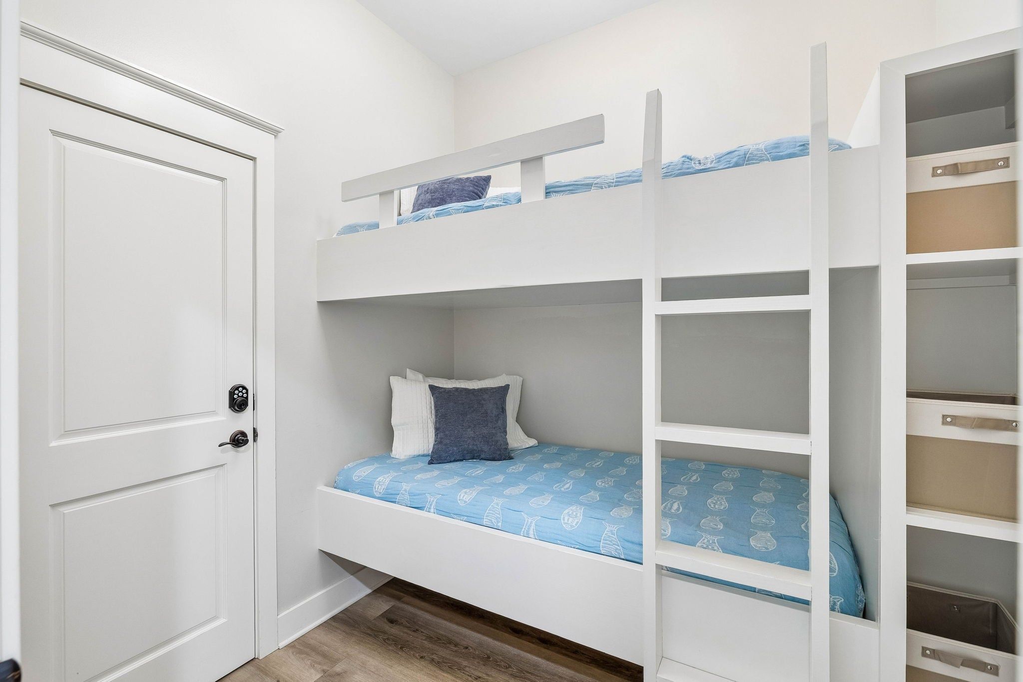 Un lit superposé avec un lit inférieur, une porte avec une serrure et une armoire blanche avec des étagères ouvertes.