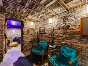 A rustic room with stone walls, wooden ceiling beams, and two teal upholstered chairs. - Historic Manor w/ Hidden Speakeasy, 3BR/2.5BA (Heber City)