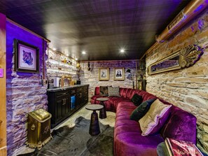 A room with a stone wall, a red velvet sofa, a bar area with shelves, and a framed picture of a leopard. - Historic Manor w/ Hidden Speakeasy, 3BR/2.5BA (Heber City)