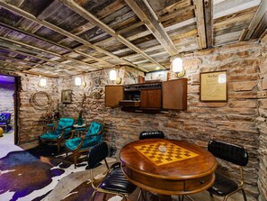 A rustic interior with stone walls, wooden beams, a checkered table, and leather chairs. - Historic Manor w/ Hidden Speakeasy, 3BR/2.5BA (Heber City)