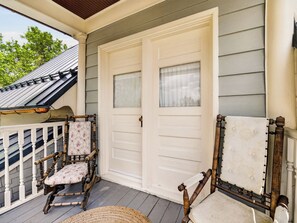 Een veranda met twee schommelstoelen, een witte deur en een overdekt gedeelte met een metalen dak.