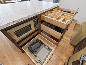 Een keuken met een inbouwmagnetron, een lade met keukengerei en een aanrecht.
