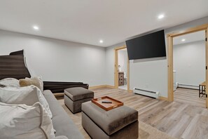 Ein modernes Wohnzimmer mit einer Couch, einem Hocker und einem an der Wand befestigten Flachbildfernseher.