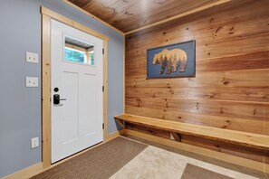 A room with a white door, a bench, and a wall-mounted bear picture. - New Bethel Retreat | Hot Tub, Pinball & Fireplace (Bethel)