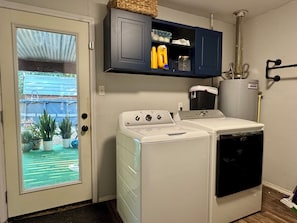 A laundry room with two washing machines, a cabinet above, and a door leading to a balcony with potted plants.