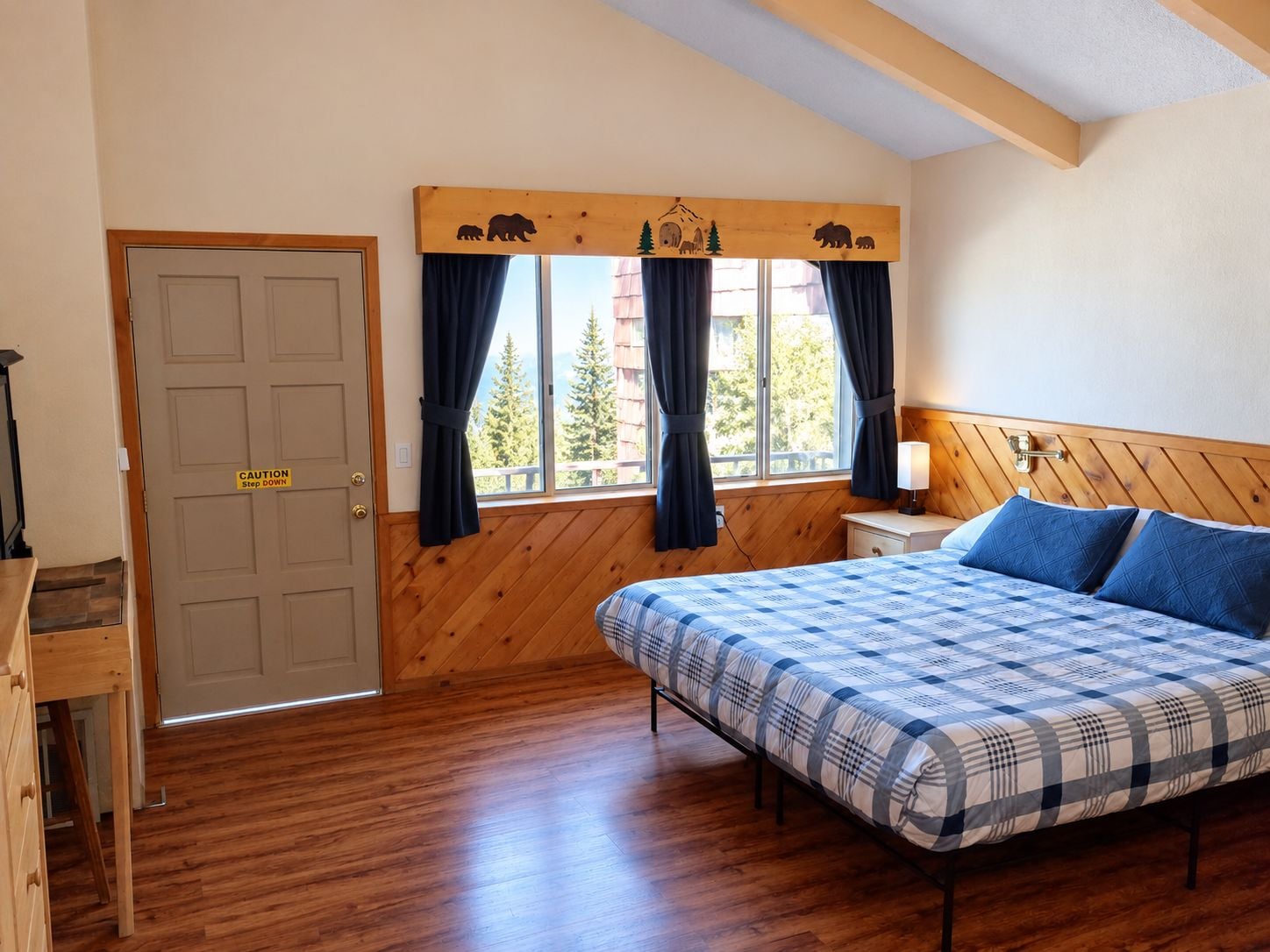 Una habitación con una cama, una mesita de noche, una puerta de madera y una ventana con cortinas.