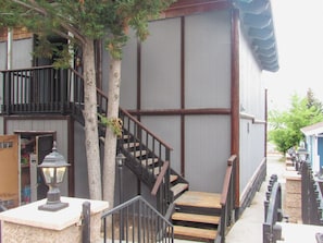 A building with a wooden staircase, metal railings, and a tree in front.