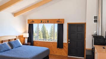 A bedroom with a bed, a window with curtains, a door, and a fireplace.
