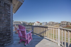 A wooden deck with a pink Adirondack chair, overlooking a coastal residential area with multiple houses. - 5472 - Azure Dreams Oceanside (Nags Head)