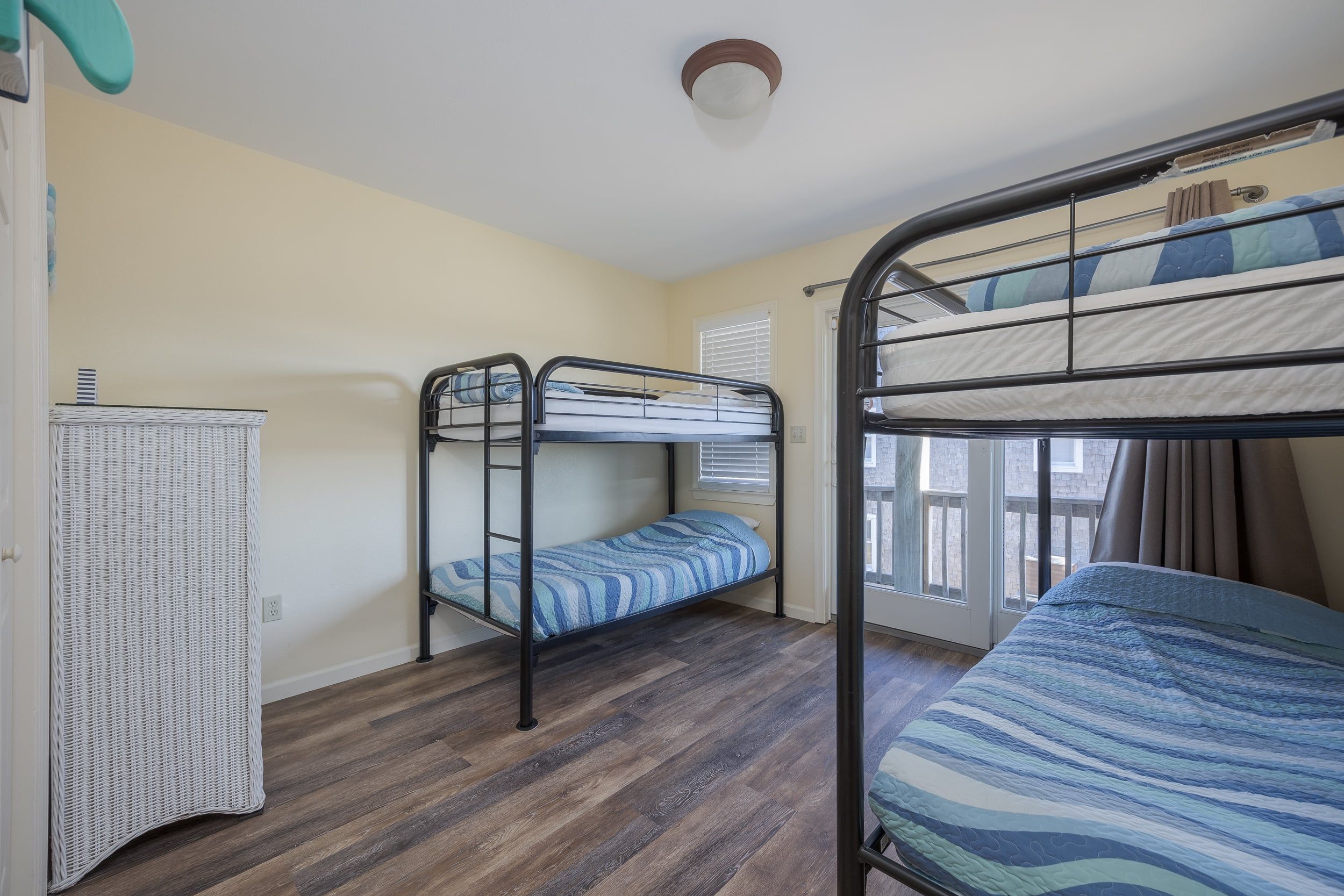 A room with two bunk beds, a small cabinet, and a window with blinds.