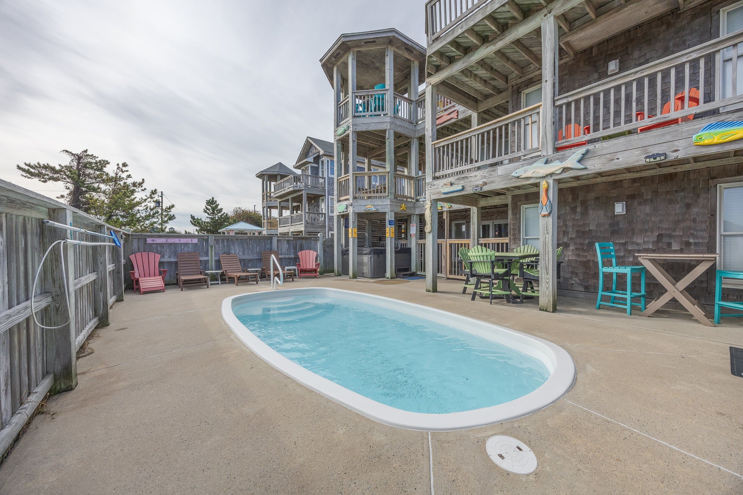A pool area with a wooden deck, lounge chairs, and a multi-level building with balconies.