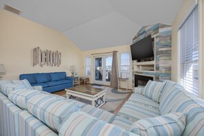 A living room with a blue sofa, striped cushions, a coffee table, a flat-screen TV, and a fireplace. - 5472 - Azure Dreams Oceanside (Nags Head)