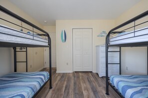 A room with two bunk beds, a white door, and a wall decoration. - 5472 - Azure Dreams Oceanside (Nags Head)