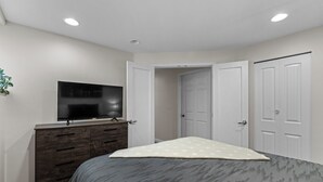 Un dormitorio con cama, cómoda, televisor y puerta.