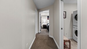 Un pasillo con piso alfombrado, una puerta que da a un dormitorio y una zona de lavandería con lavadora.