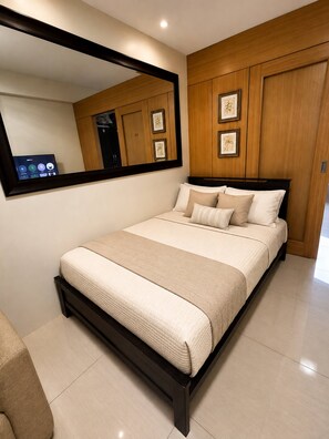 A modern bedroom with a large bed, a wall-mounted mirror, and framed artwork. - Modern 2-bedroom Apartment With Shared Pool in Central Pasay (Pasay)