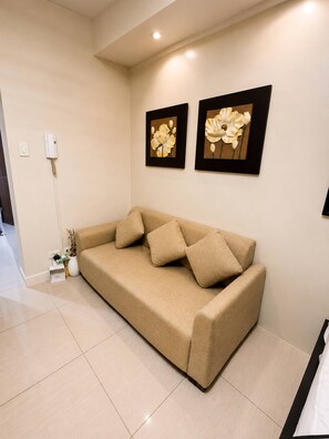 Ein beiges Sofa mit Kissen, ein kleiner Beistelltisch mit einer Vase und zwei gerahmte Blumenbilder an der Wand.