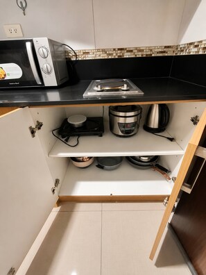 A compact kitchen with a microwave, stove, and various pots and pans stored on shelves. - Modern 2-bedroom Apartment With Shared Pool in Central Pasay (Pasay)