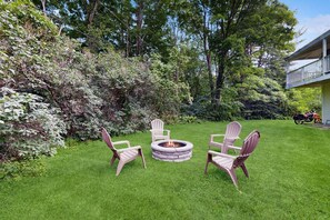 A well-maintained grassy area with a stone fire pit and Adirondack chairs.