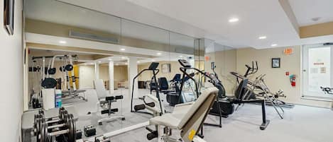 A modern gym with various exercise equipment, a mirrored wall, and a visible exit sign.