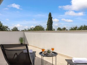Ein Balkon mit Stuhl, einem kleinen Tisch mit Getränken und Blick auf Bäume sowie einen hohen Baum.