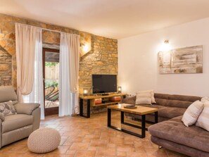 Ein Wohnzimmer mit Steinwand, Flachbildfernseher, Sofa, Couchtisch und einem gemusterten Ottomanen.
