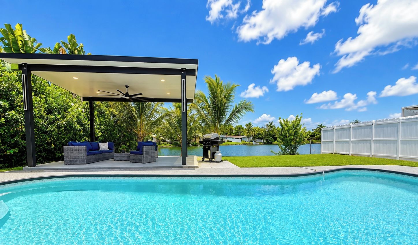 Una piscina con una zona de estar cubierta, una parrilla y vista a un lago.