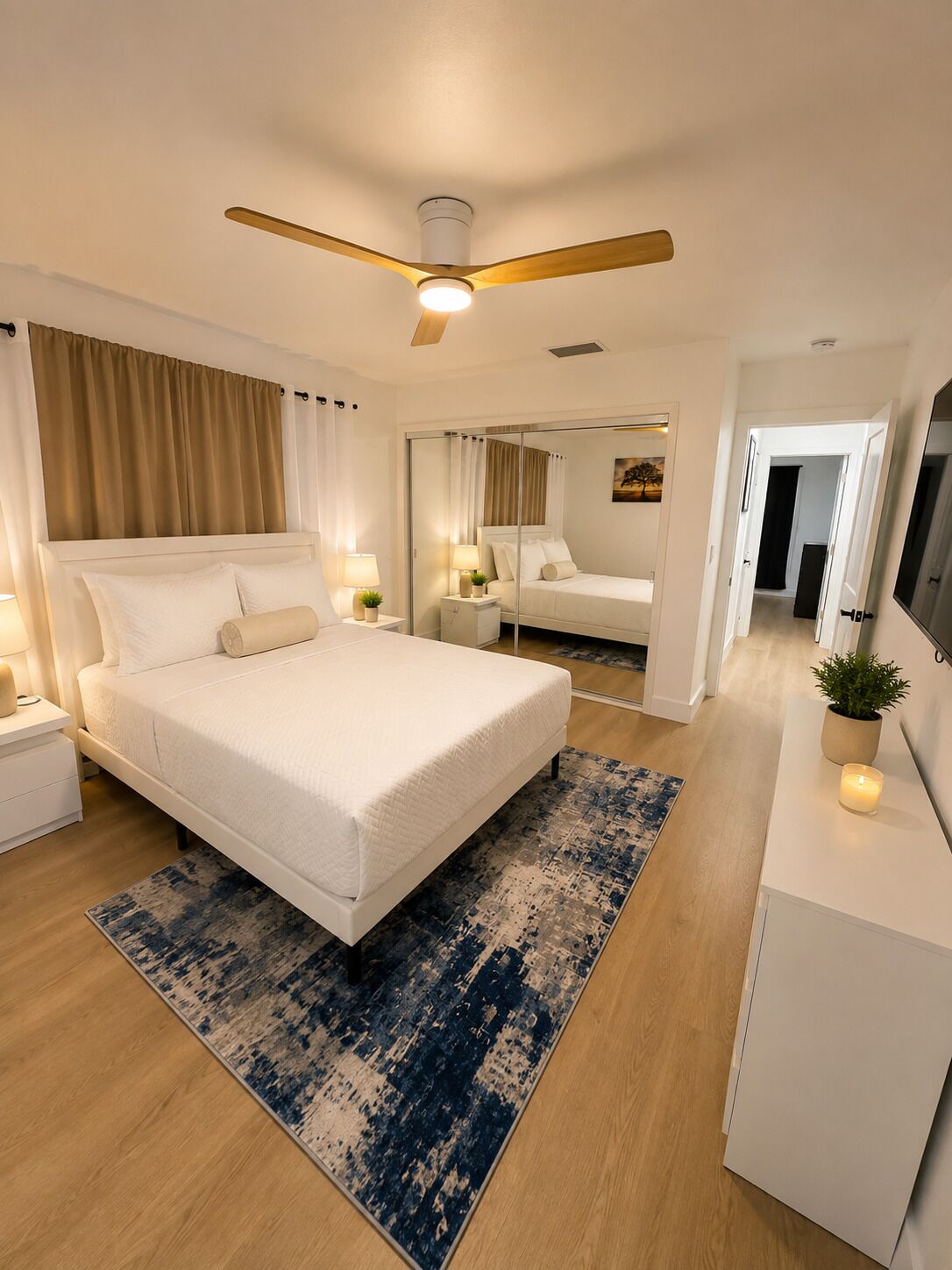A modern bedroom with a large bed, bedside lamps, a ceiling fan, and a mirror.