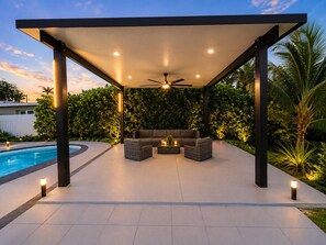Eine Terrasse im Freien mit Pool, Deckenventilator und einer Sitzgelegenheit mit Kissen.