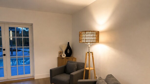 Uma sala de estar com um sofá cinza, uma poltrona cinza, um abajur e uma mesa lateral de madeira.