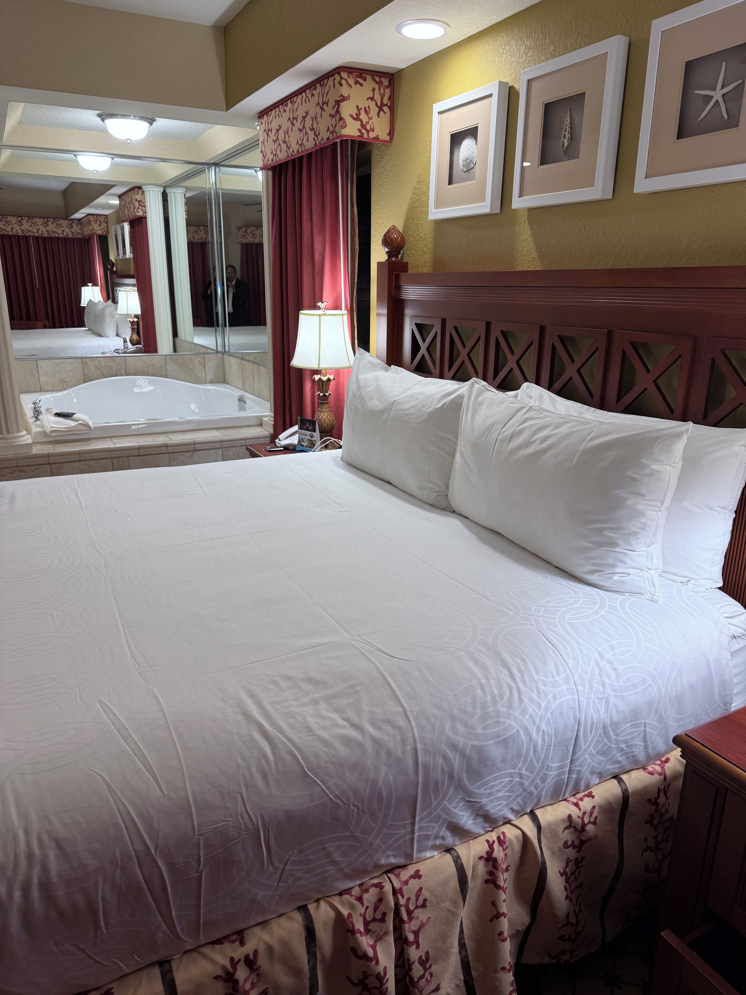 Ein Hotelzimmer mit einem großen Bett, einem Nachttisch, einer Lampe, einem Spiegel und einem Bilderrahmen an der Wand.