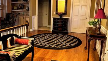 Un vestíbulo bien iluminado con piso de madera, un tapete estampado, una silla con cojín, una lámpara y un espejo sobre una consola.