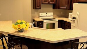 Una cucina con mobili in legno scuro, piano cottura bianco, frigorifero bianco e isola centrale con sedie.