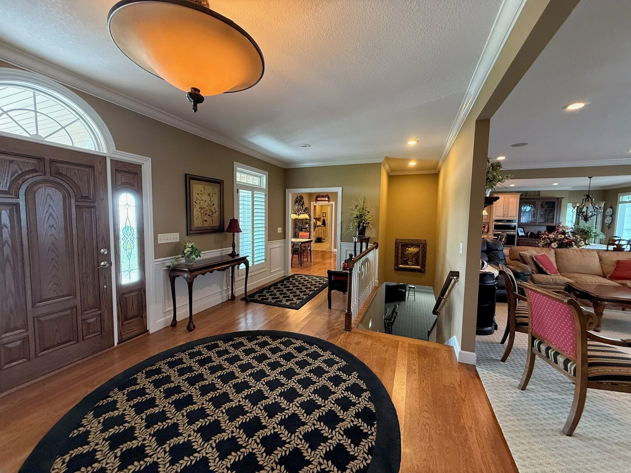 A spacious living area with a large rug, wooden flooring, and a staircase leading to another level.
