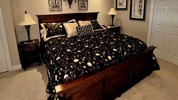 Un dormitorio con una cama grande, dos mesitas de noche, una lámpara de techo, una planta en maceta y obras de arte enmarcadas en las paredes.