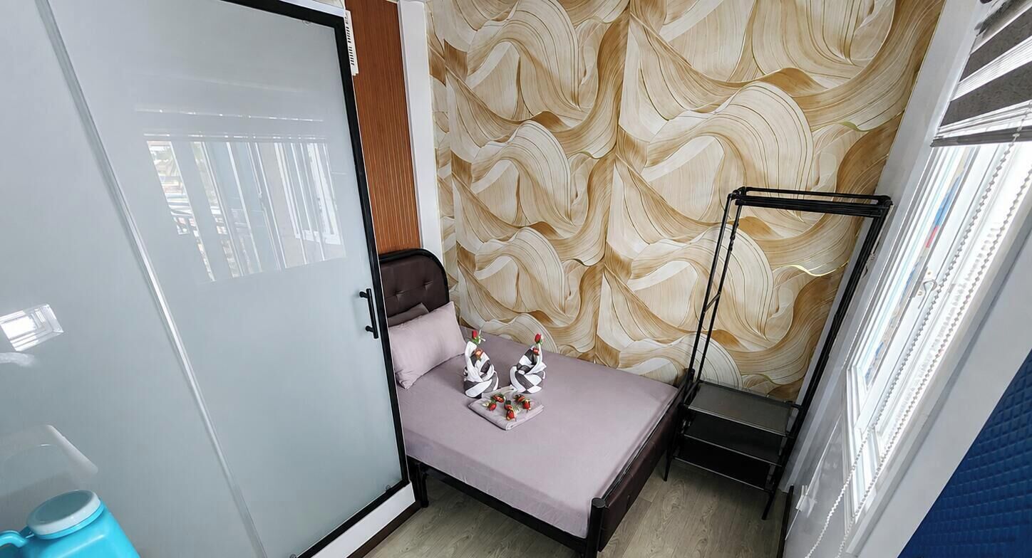 Une petite pièce comprenant un lit, une armoire, une fenêtre avec des stores et un mur décoré d’un motif.