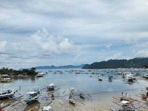 Uma marina costeira com diversos barcos atracados, paisagem acidentada ao fundo e céu nublado.