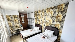 A hotel room with two beds, a small table with chairs, a decorative wall, and a window.