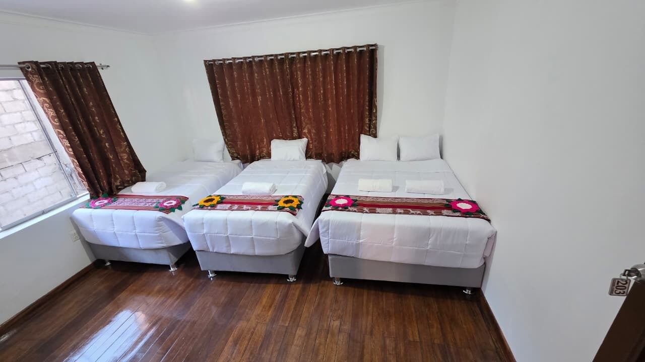 A room with three beds, a window with curtains, and a wooden floor.